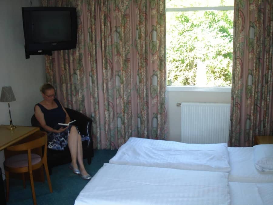 A hotel room with a bed, a desk with a lamp, a television, and floral curtains.