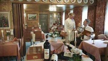 A dining area with tables set for a meal, a bottle of wine, and a bouquet of flowers on the table.