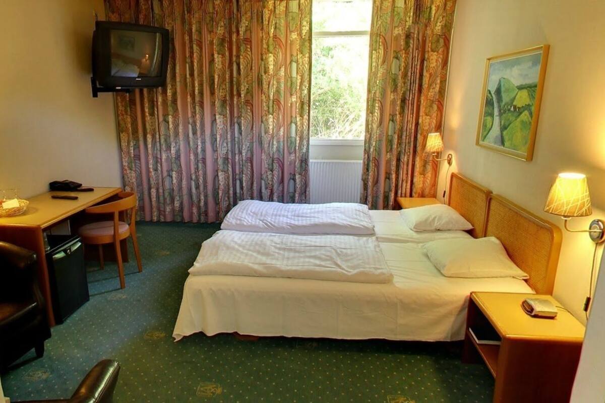 A hotel room with a bed, a desk with a chair, a television, and a painting on the wall.