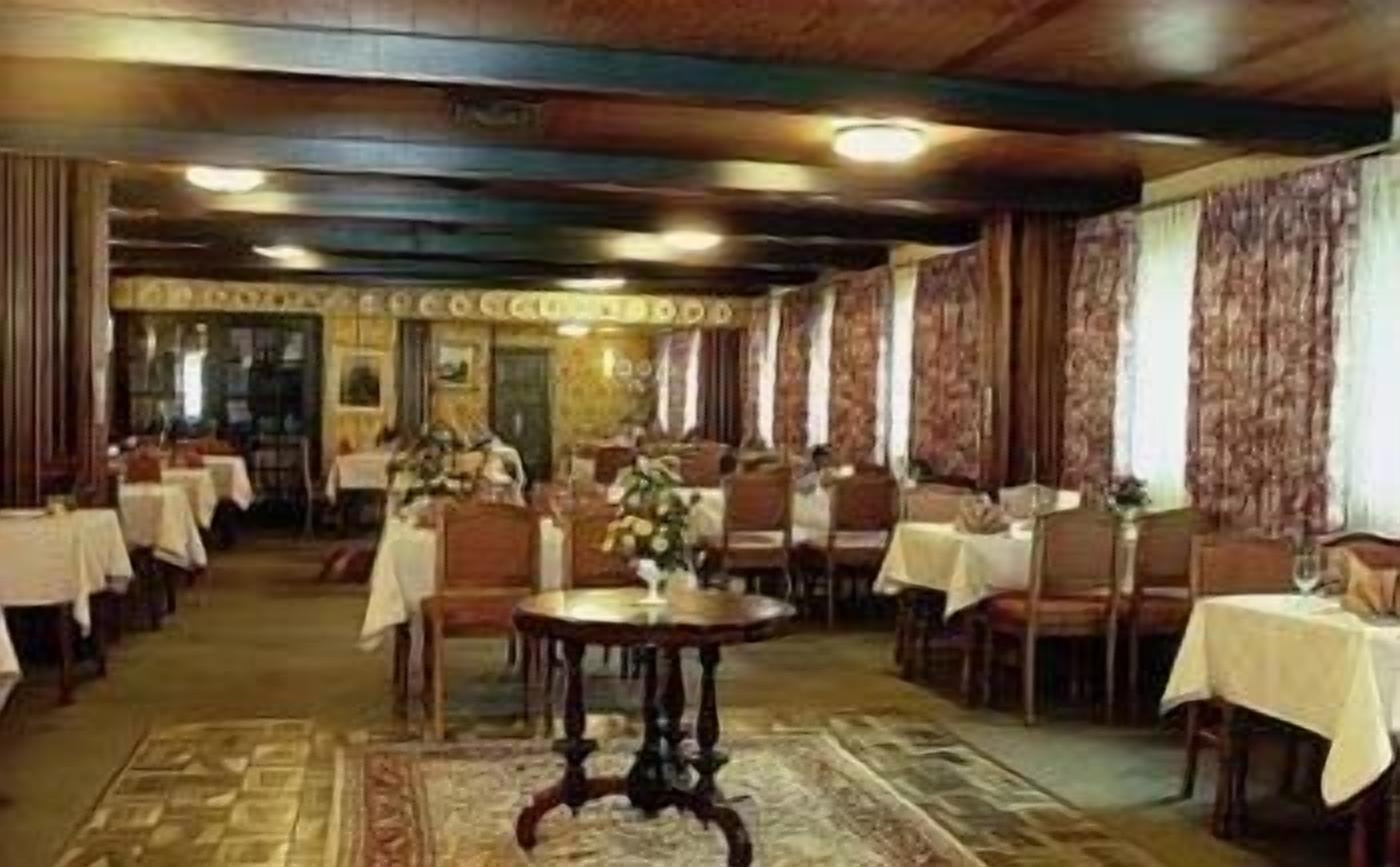 A dining area with multiple tables and chairs, a central round table with a vase, and a patterned carpet.