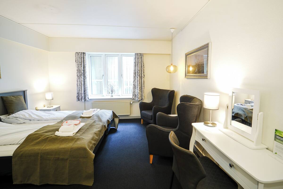 A hotel room with two beds, a desk with a computer, a chair, a lamp, and a window with curtains.
