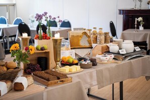 Montaje de un bufé de desayuno con diversas opciones de comida, como frutas, quesos y panes, sobre una mesa cubierta con un mantel.