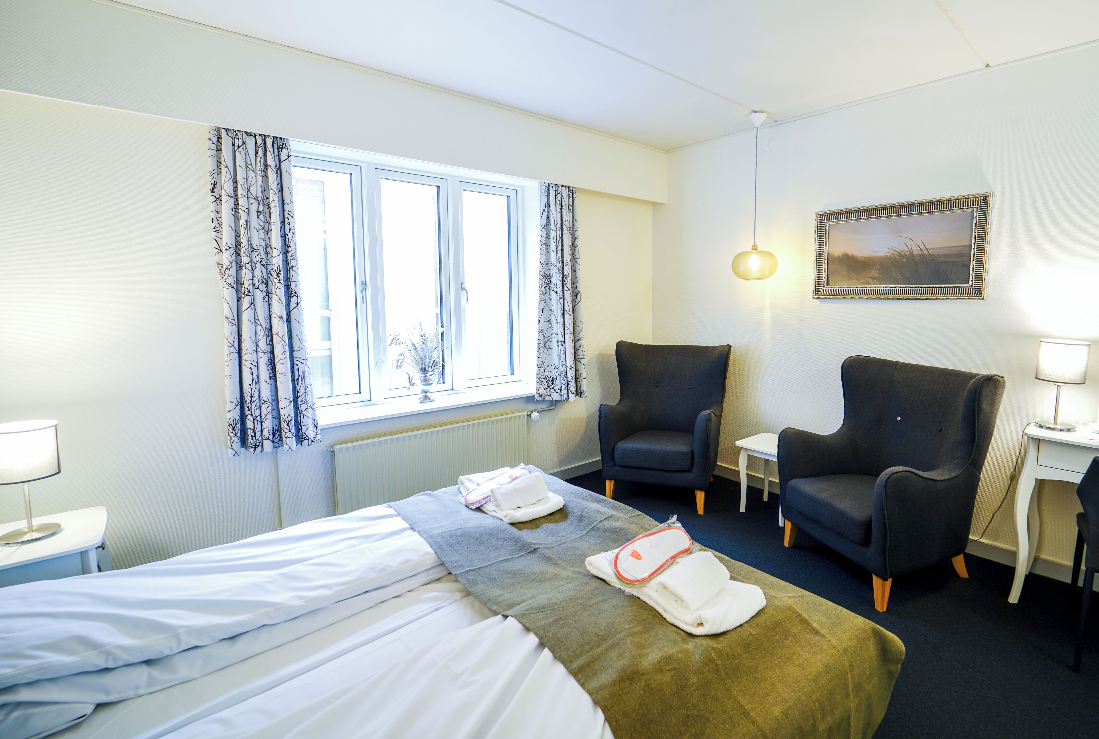 Habitación de hotel con cama, dos sillones, una mesita, una lámpara y un cuadro en la pared.