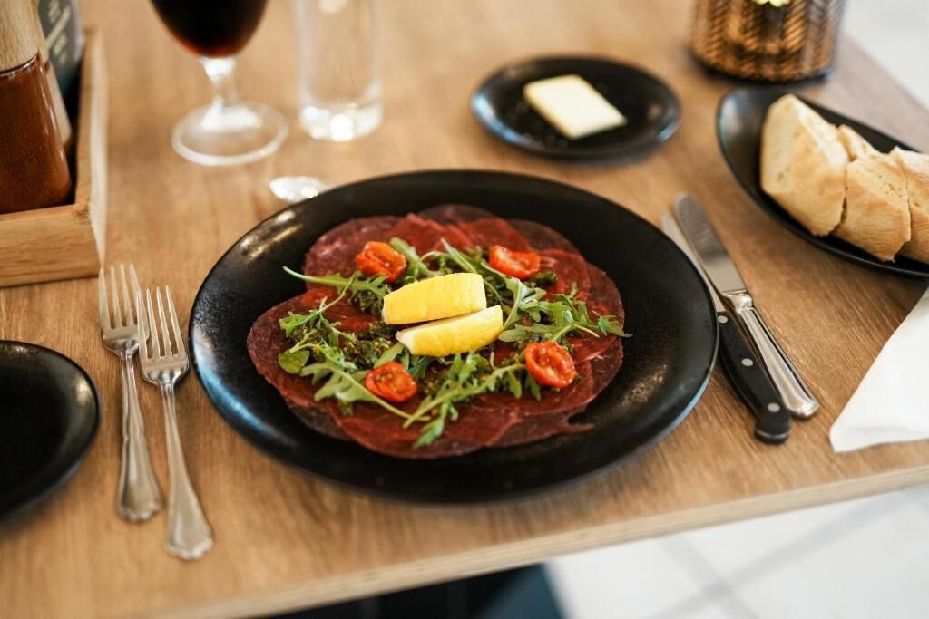 A plate of food with a black rim, garnished with tomatoes and greens, on a wooden table.