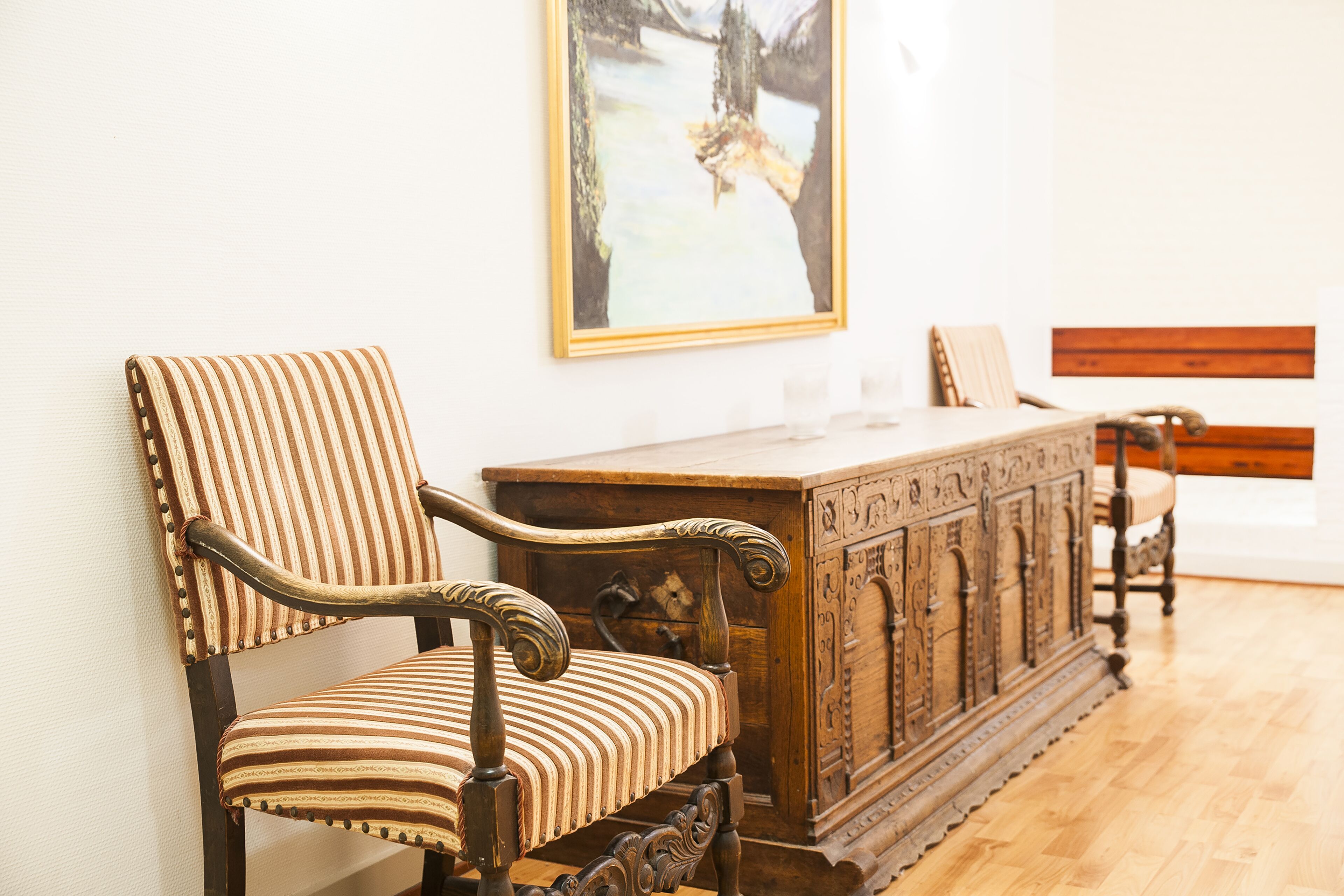 A room with a wooden cabinet, a striped upholstered chair, and a bench.