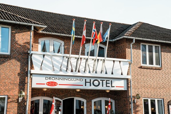 Un hotel con un cartel que dice 'Dronninglund Hotel' y varias banderas en el tejado.
