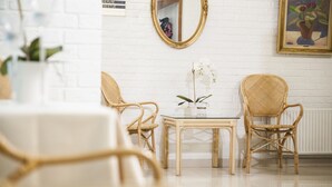 A room with white brick walls, a round mirror, two wicker chairs, a small table, and a potted orchid. - Dronninglund Hotel (Dronninglund)