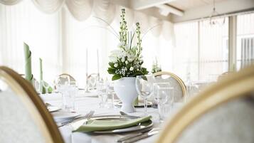 Una mesa de comedor dispuesta con mantel blanco, servilletas verdes y un jarrón blanco con flores.
