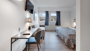 Een moderne hotelkamer met een bed, een bureau met stoel, een aan de muur bevestigde televisie en een raam met gordijnen.