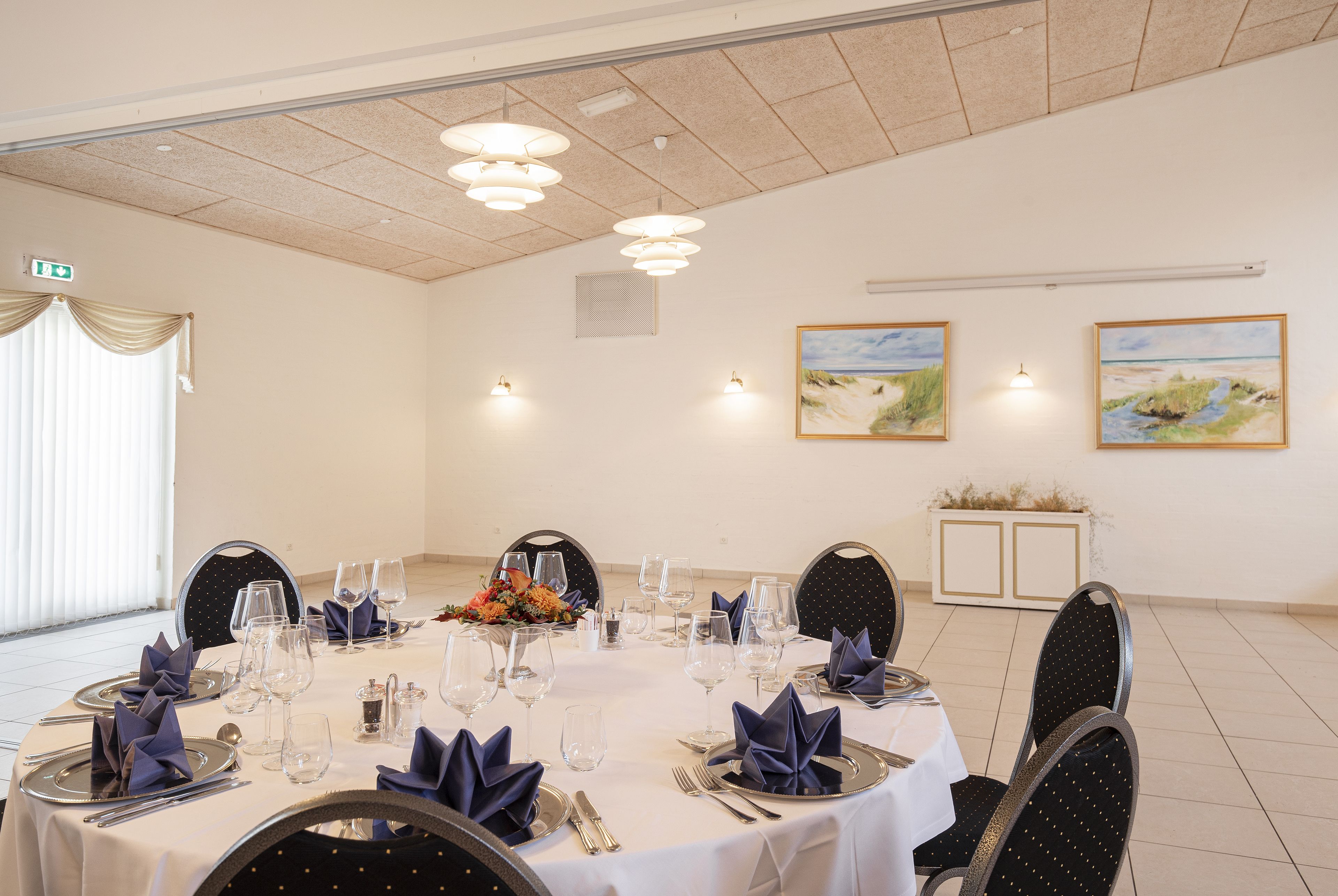 A conference room with a round table set for a formal event, equipped with chairs, tables, and lighting fixtures.