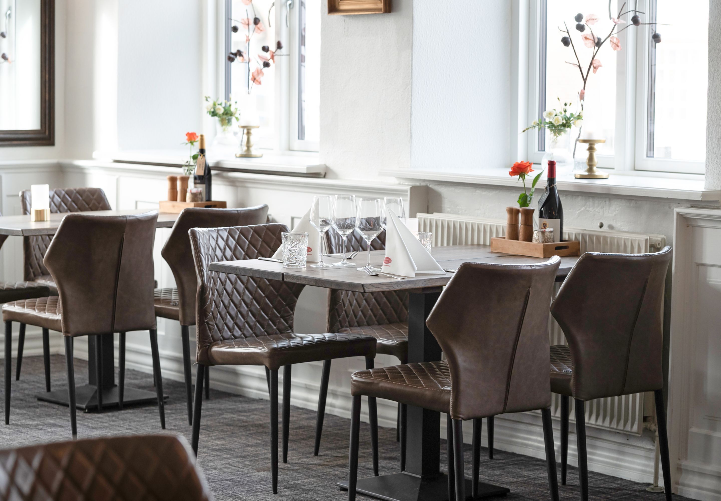 Un espace repas comprenant plusieurs tables et chaises, aménagé dans un décor moderne avec de grandes fenêtres et des fleurs décoratives.