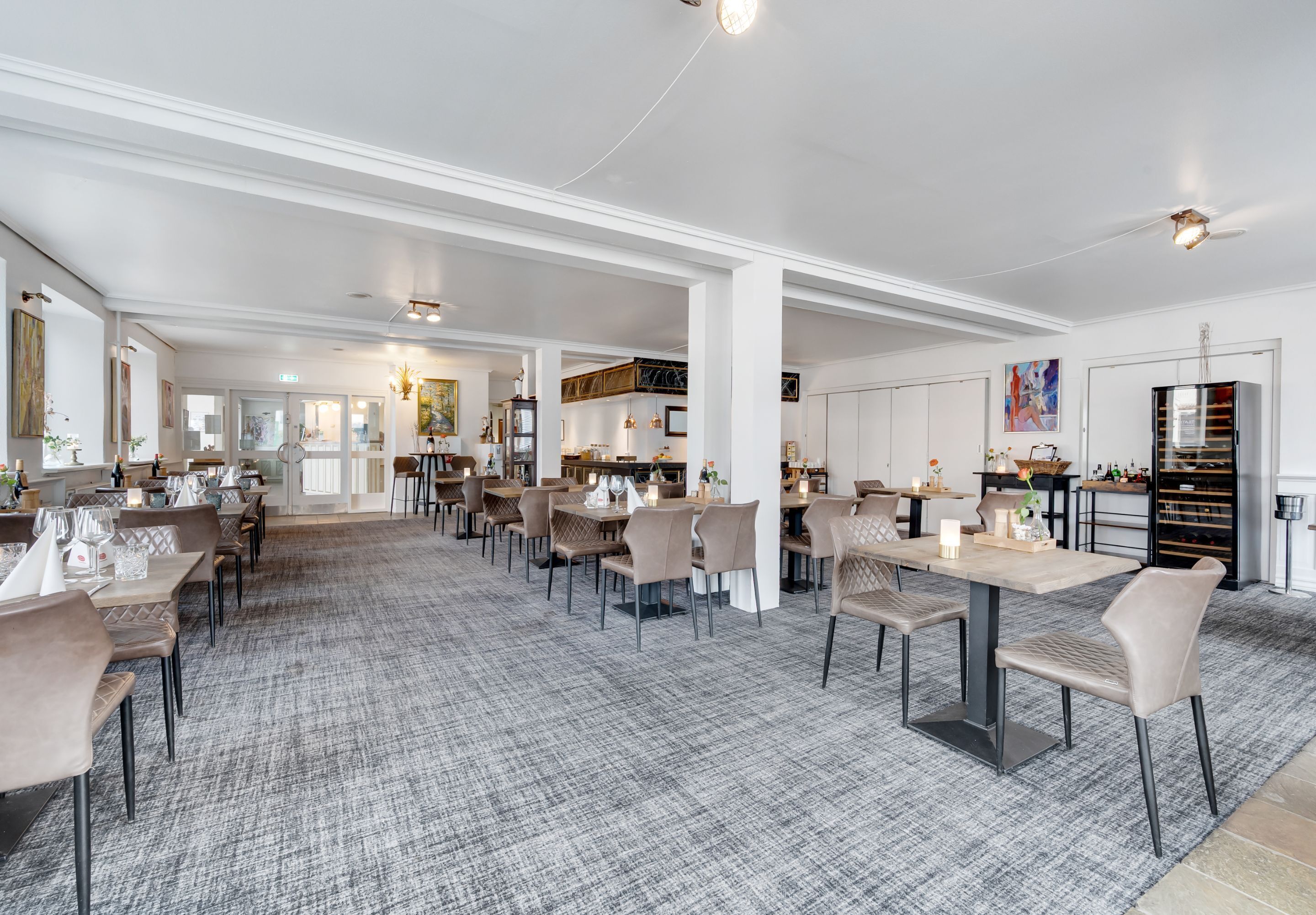 En rummelig spiseafdeling med flere borde og stole, et mønstret tæppe og et moderne loftdesign.