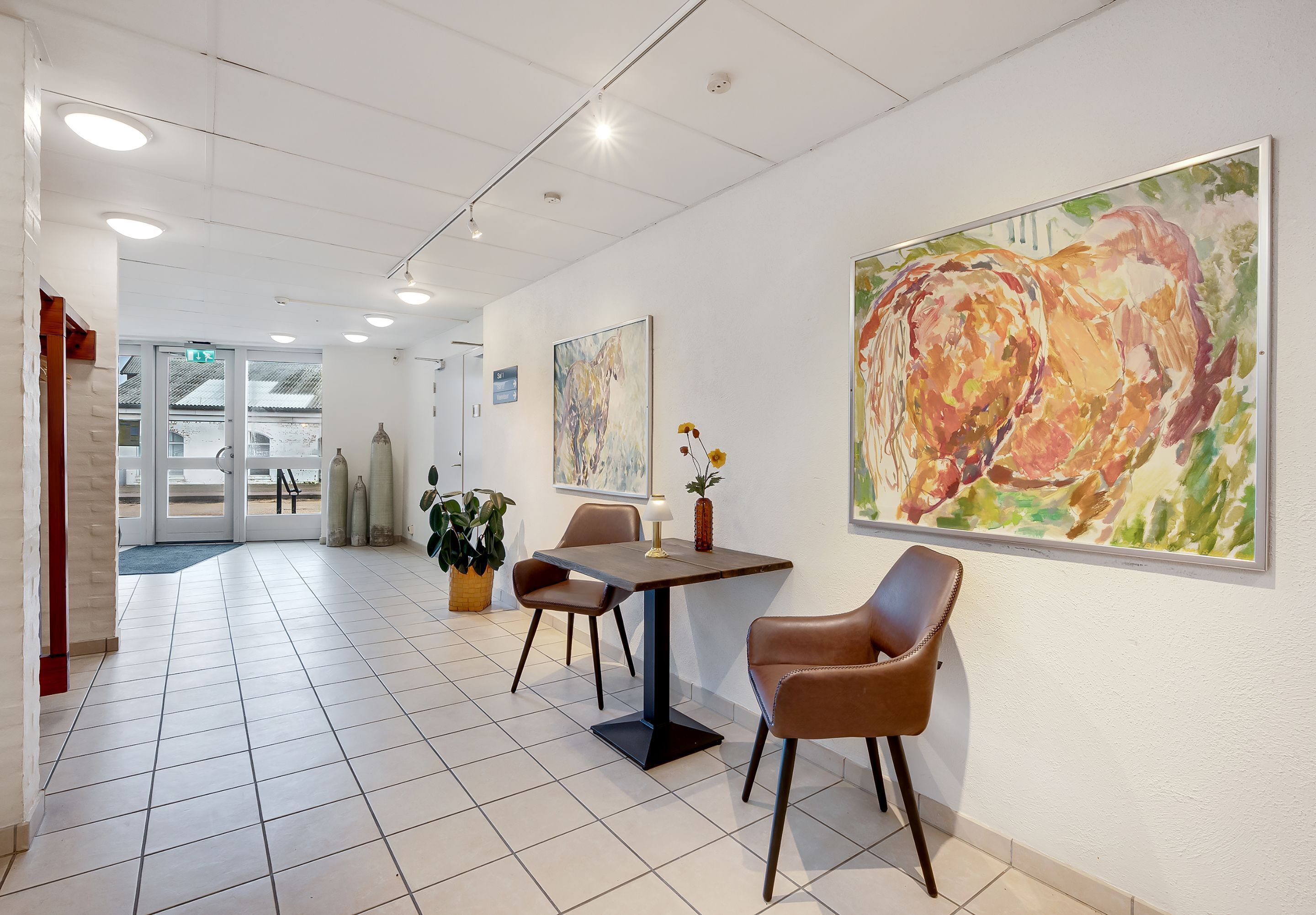 A modern interior with a dining area featuring a table and chairs, a potted plant, and two large abstract paintings on the wall.