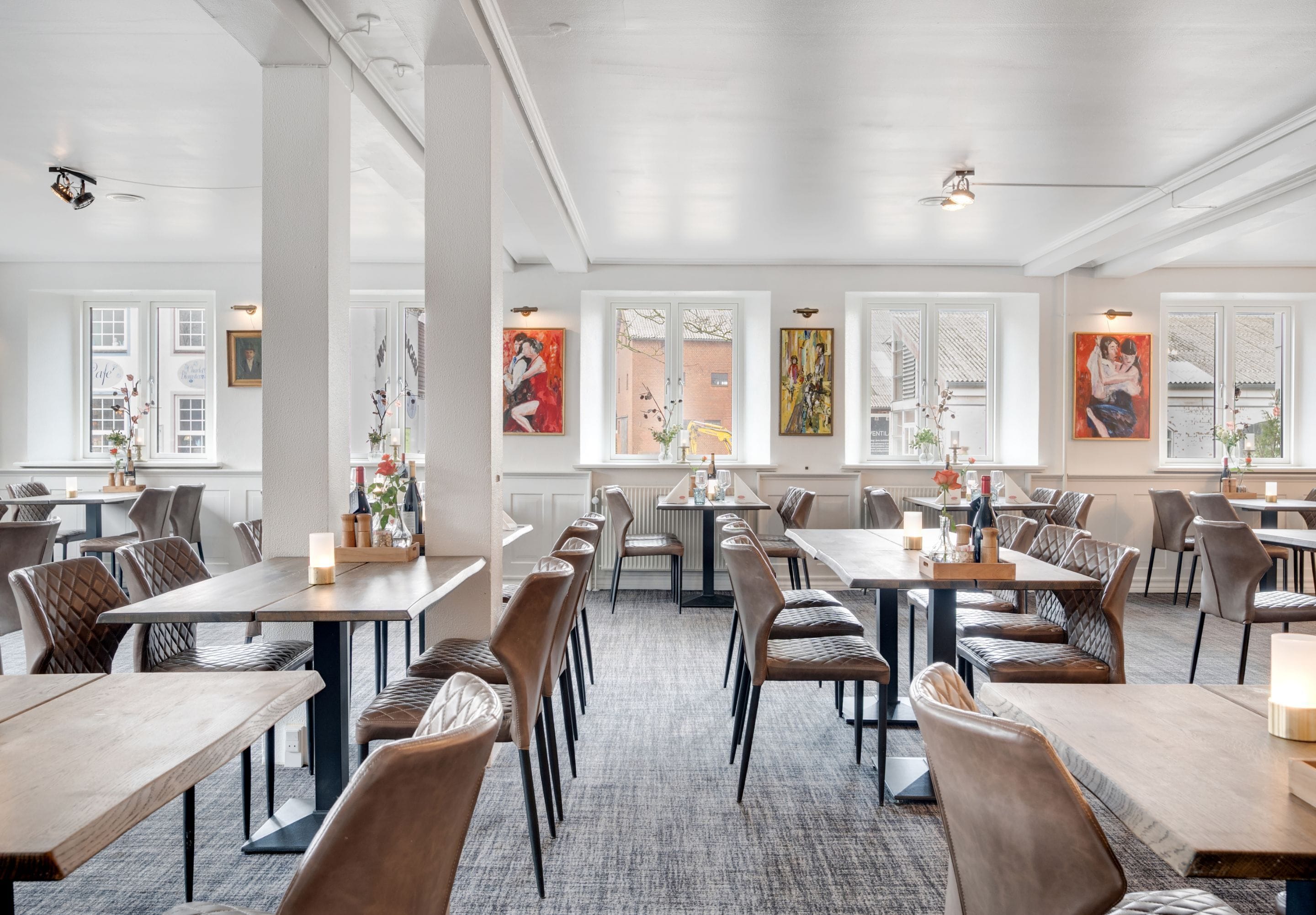 Un vaste espace dédié à la salle à manger, avec de nombreuses tables et chaises, de grandes fenêtres et des œuvres d’art accrochées aux murs.
