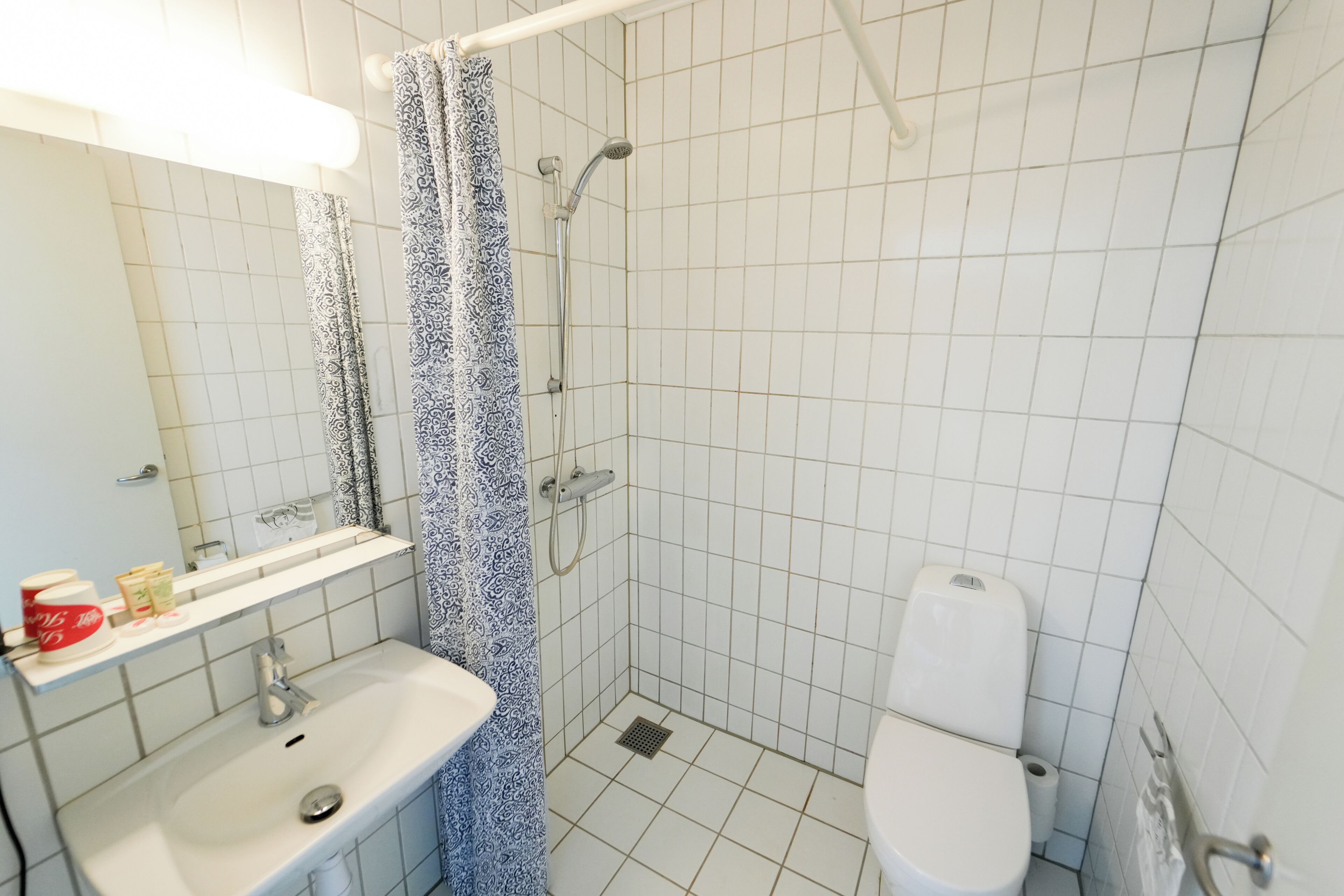 A bathroom with a shower, toilet, sink, and a mirror.