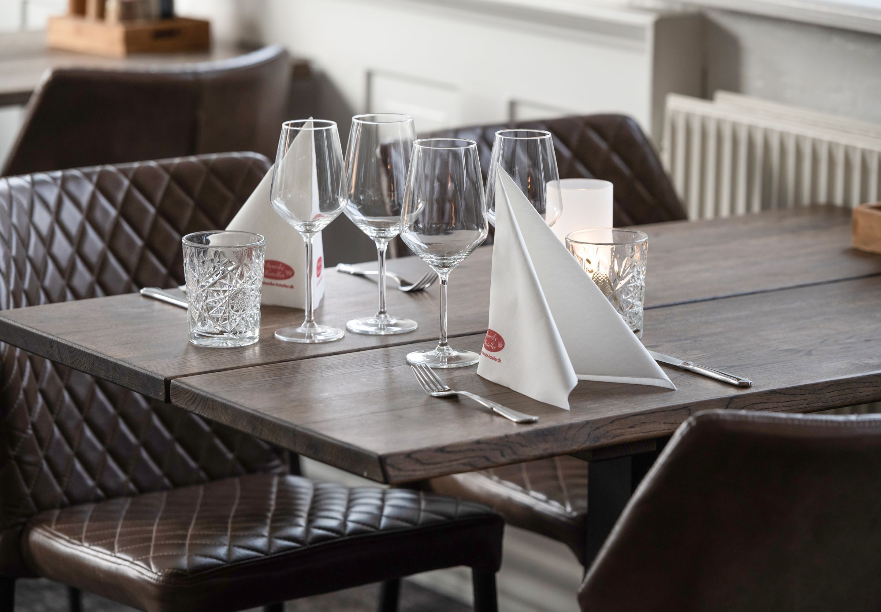 Une table à manger dressée avec plusieurs verres à vin, une bougie et un menu.