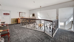Een ruime hotel lobby met een hoge plafond, een decoratieve smeedijzeren balustrade, een receptiebalie en een trap naar de verdiepingen erboven.