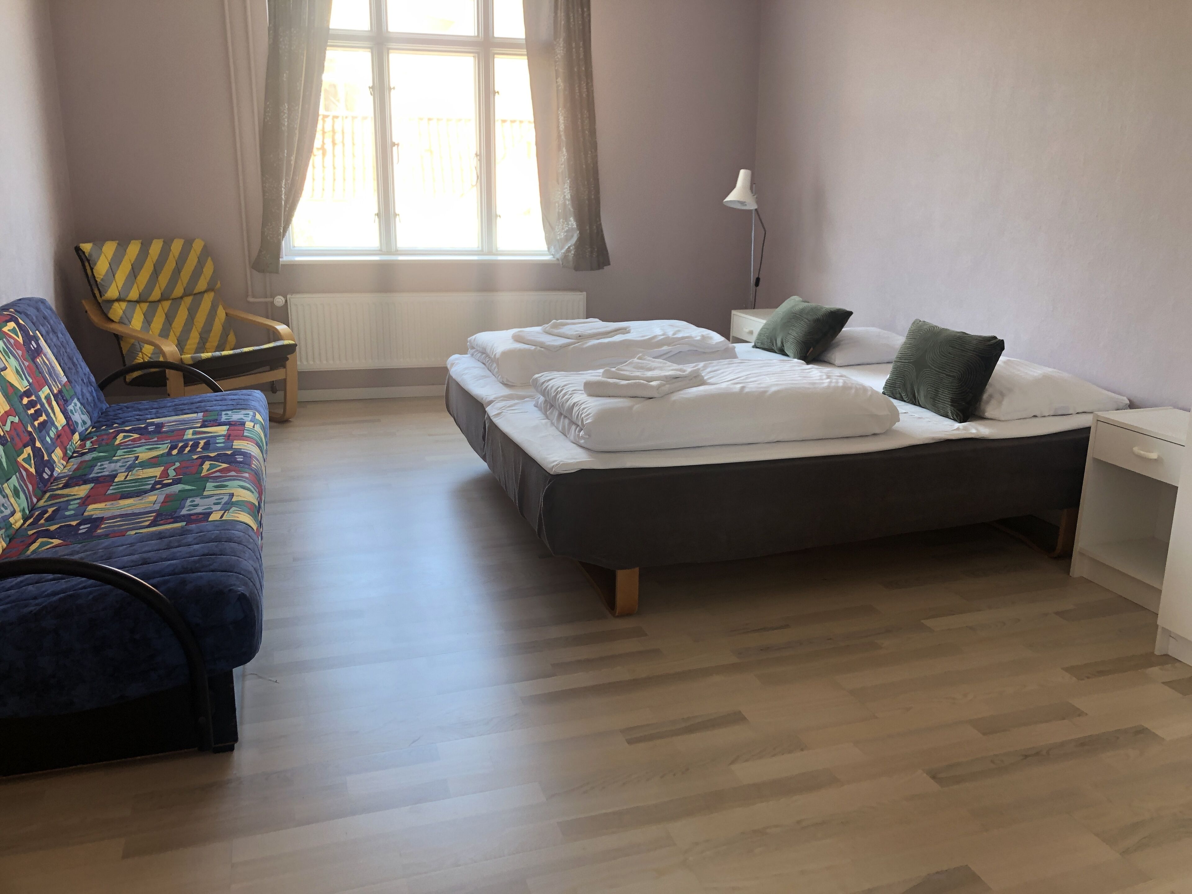 Une pièce comprenant un lit, un canapé, une chaise, une table de chevet et une fenêtre avec des rideaux.
