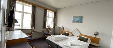 A hotel room with a bed, a desk, a chair, a TV, and a painting on the wall.