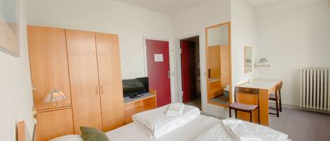 Habitación de hotel con una cama, un escritorio, una silla, un televisor y un espejo.