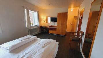 A hotel room with a bed, a desk, a chair, a TV, and a wardrobe.