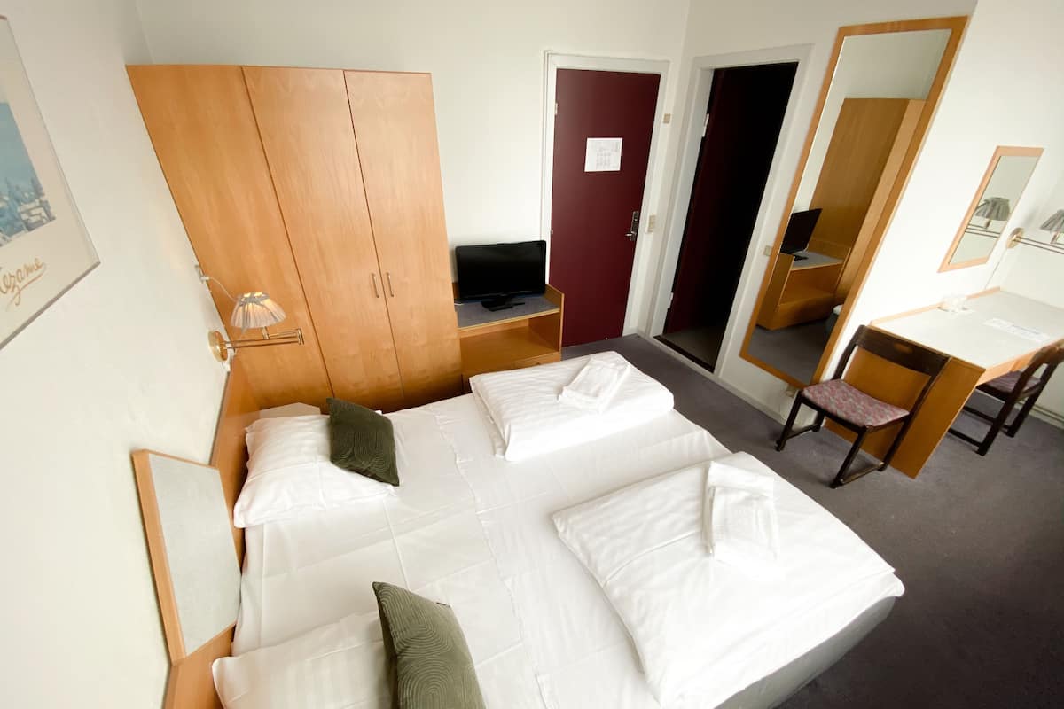 Habitación de hotel con una cama grande, un armario de madera, un escritorio con silla, televisión y espejo.