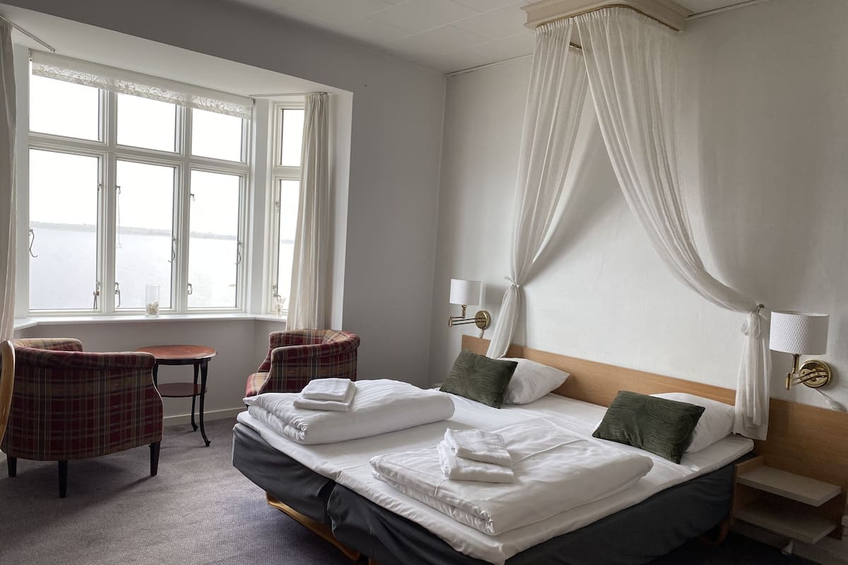 Una habitación de hotel con una cama grande, dos sillas, una mesita y una ventana con cortinas.