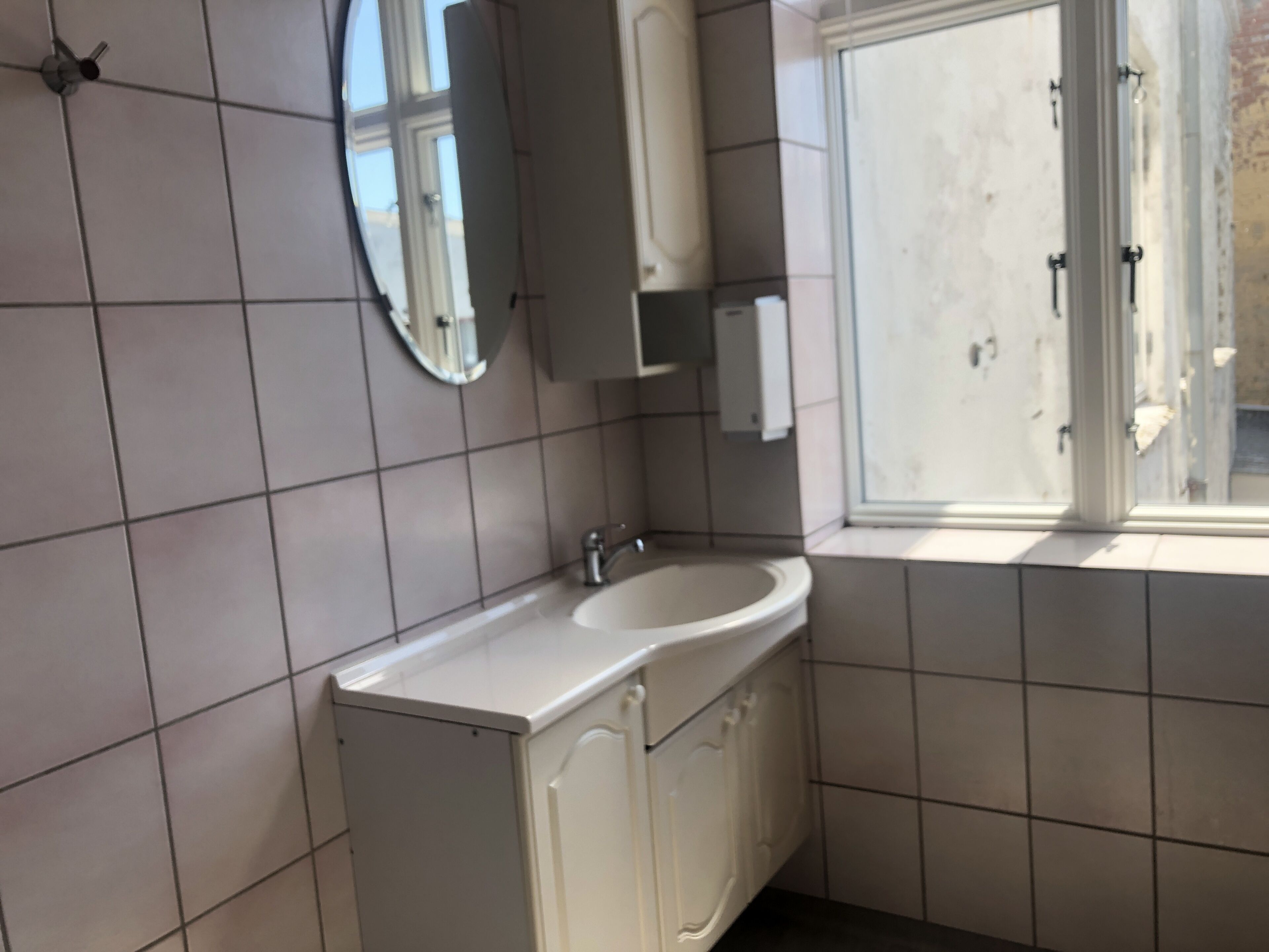 A bathroom with a white sink, a mirror, and a window.