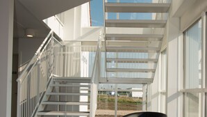 Interior moderno com escada que leva a um andar superior, uma cadeira preta e grandes janelas com vista para o exterior.