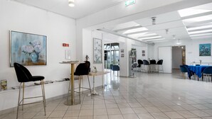 Quarto amplo e bem iluminado, com piso ladrilhado, mesa redonda com cadeiras e obras de arte nas paredes.