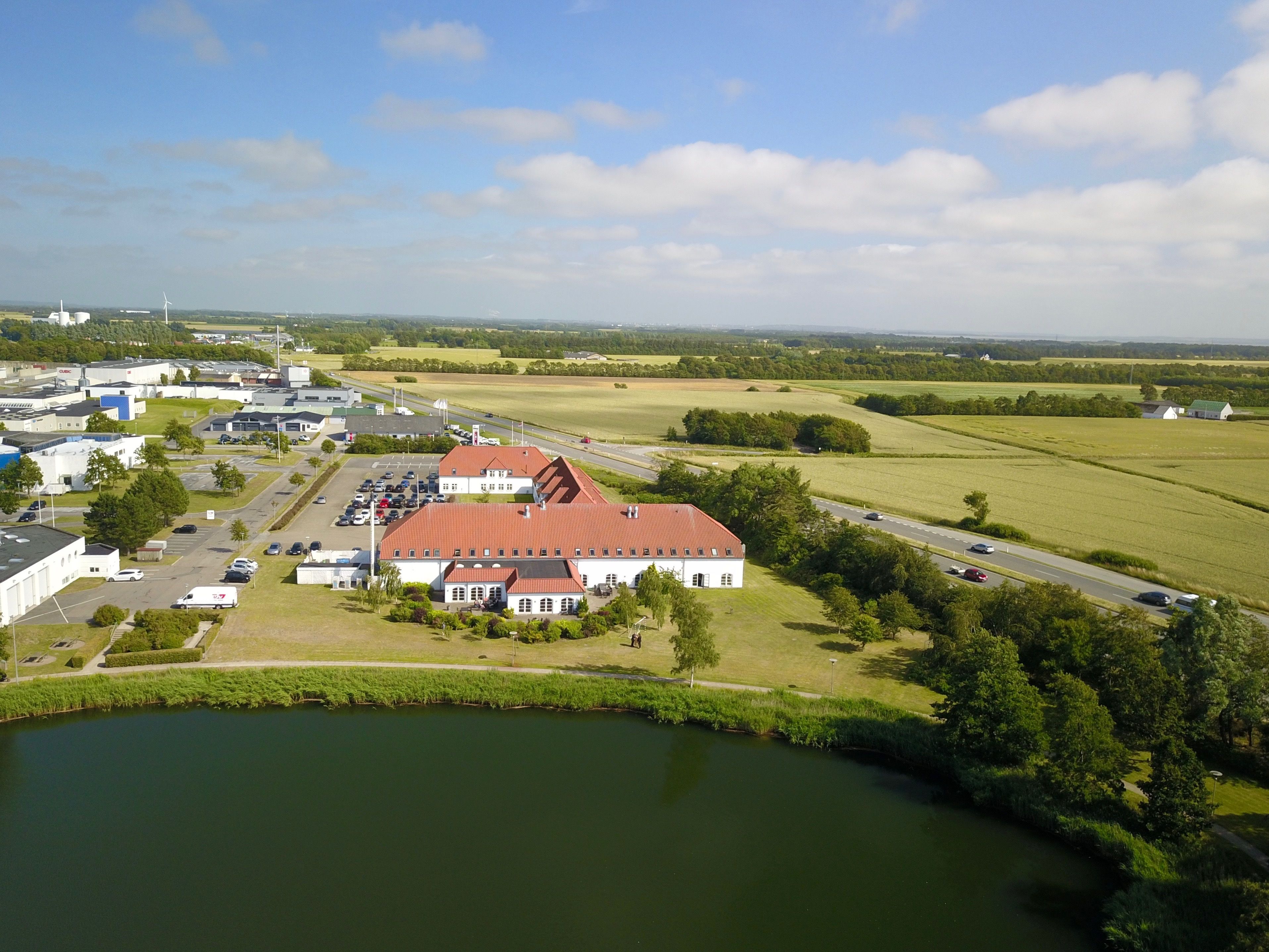 An industrial area with a large building, parking lot, and a body of water.