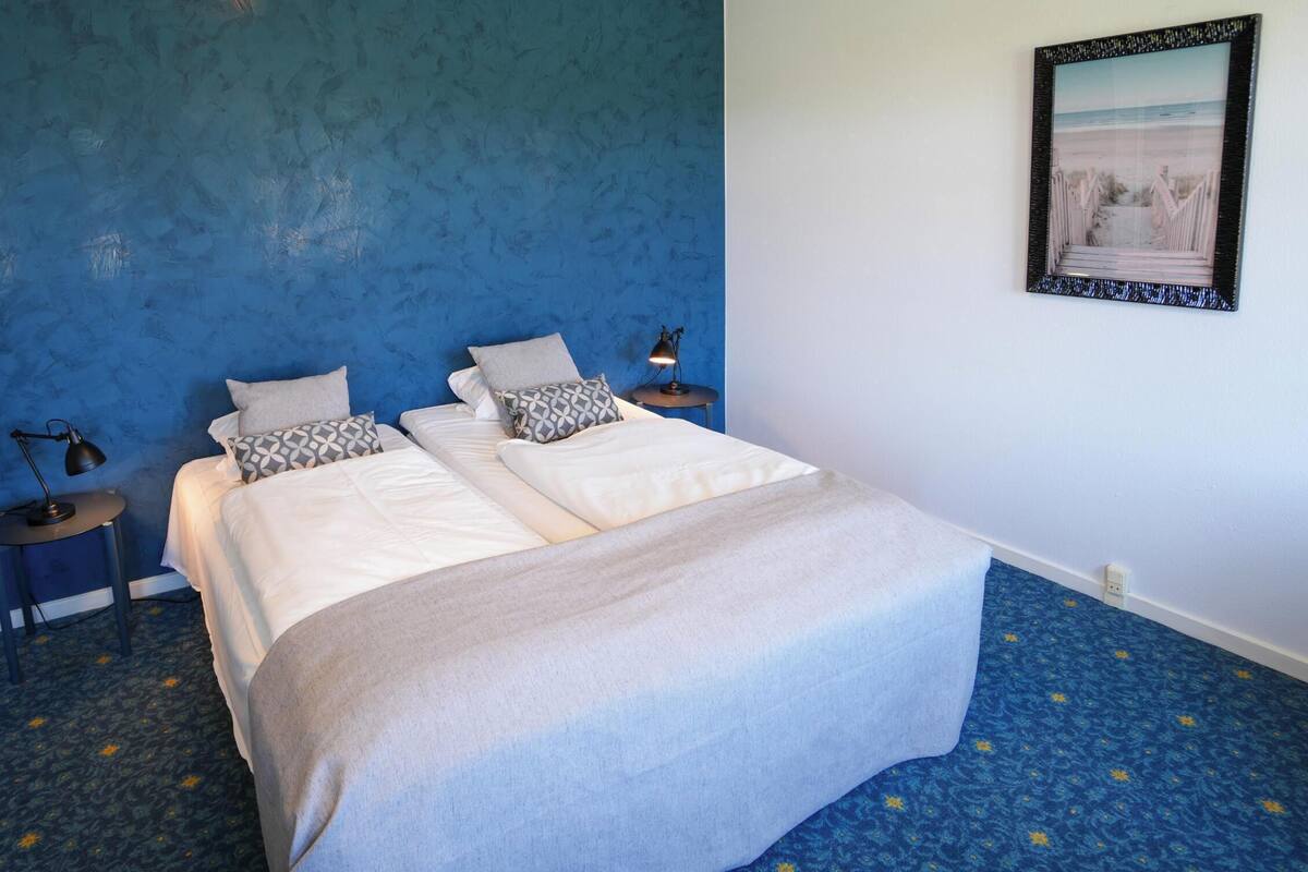 Un dormitorio con dos camas, una pared azul, un cuadro enmarcado y una alfombra estampada.