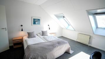 A modern bedroom with a skylight, a bed with grey bedding, a bedside table with a lamp, and a radiator.