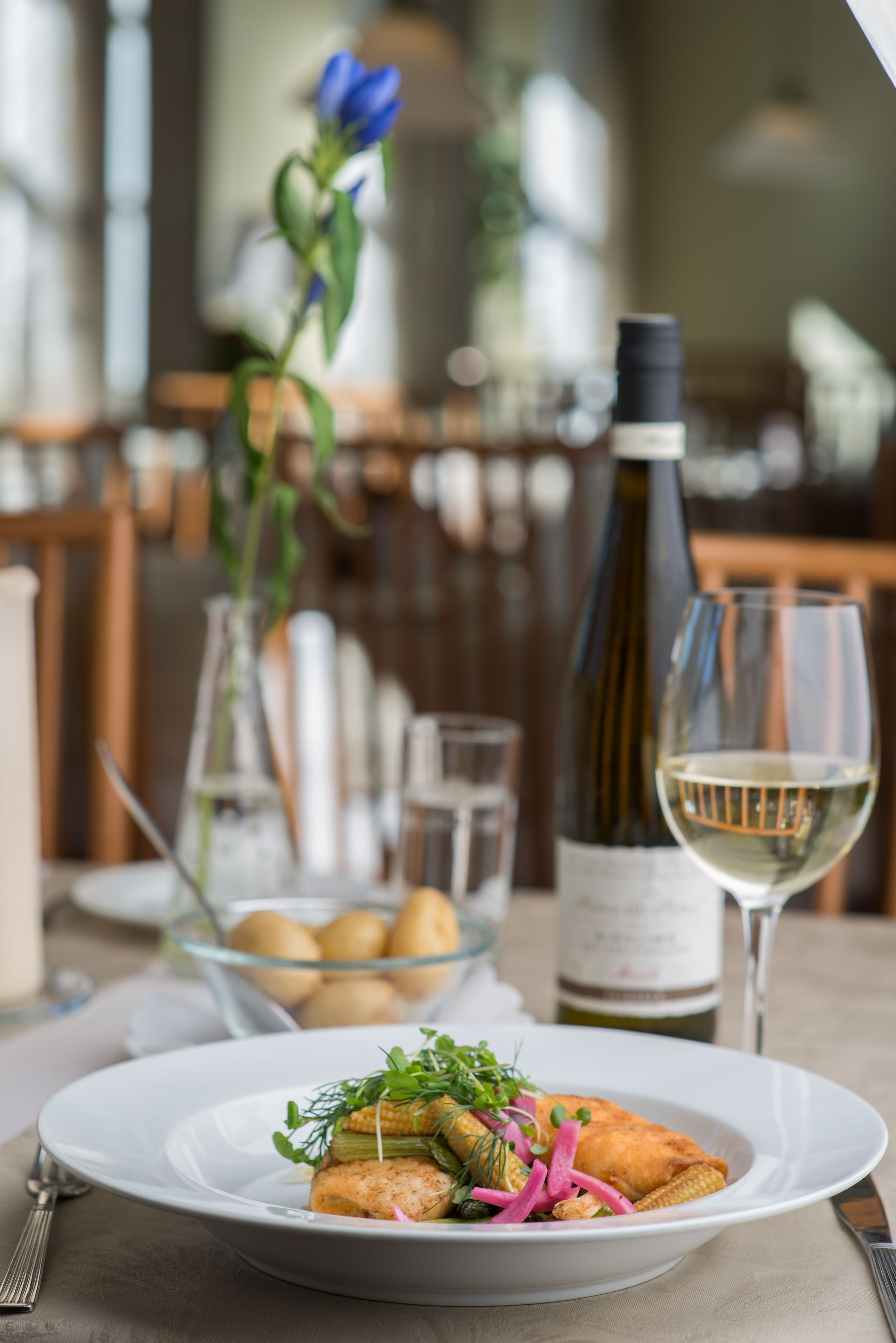 A dining table with a plate of food, a bottle of wine, and a glass of wine.