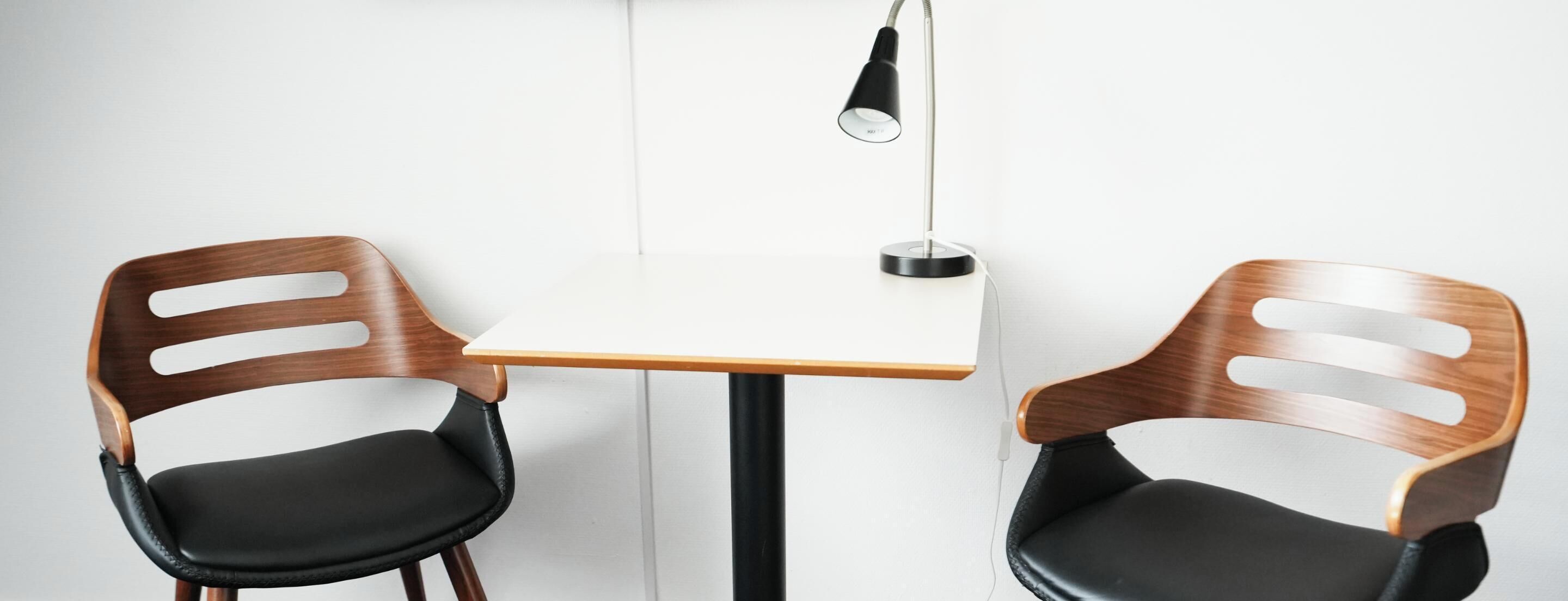 Two wooden chairs with black cushions at a white table with a black lamp.