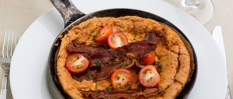 A skillet with a dish topped with bacon and tomatoes, served on a white plate.