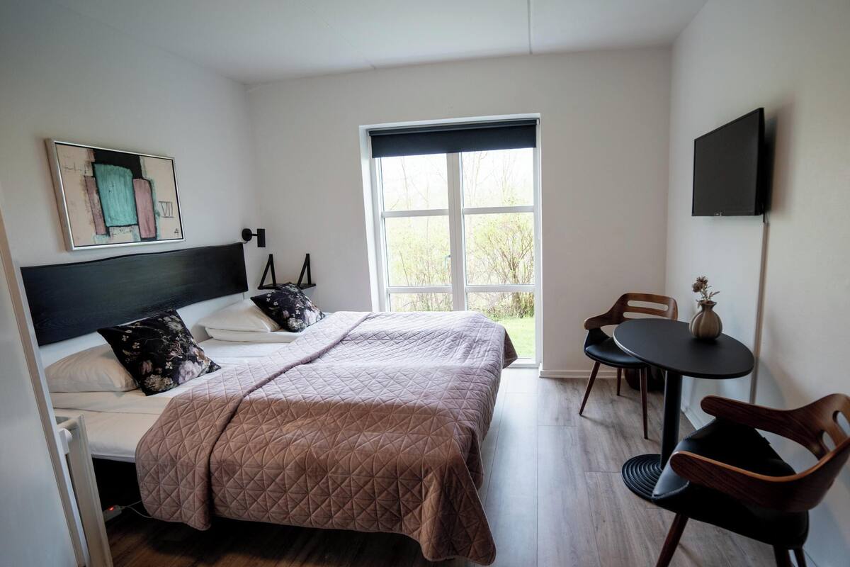 A bedroom with a bed, a window, a TV, a table, and a chair.