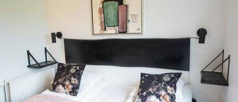 Un llit ben fet amb coixins florals, un capçaler negre i una obra d'art emmarcada a la part superior.