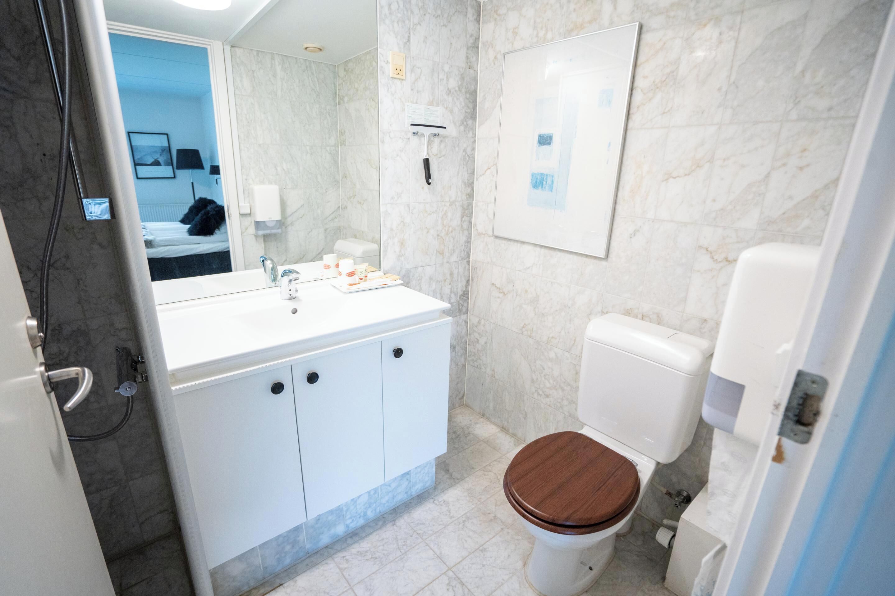 Une salle de bain moderne avec un lavabo blanc, des toilettes en bois et un mur en marbre.