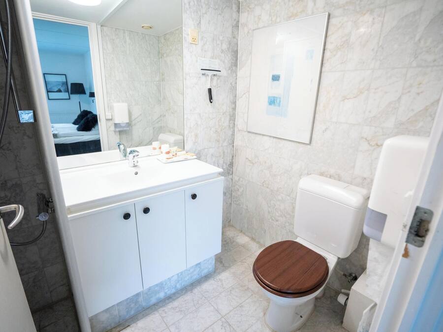 Une salle de bain moderne avec un lavabo blanc, des toilettes en bois et un mur en marbre.