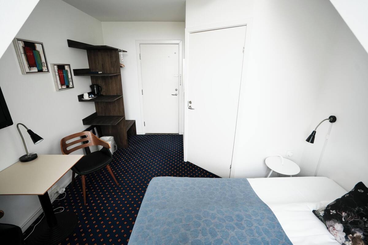 A compact room with a bed, a desk, a chair, a small table, and a bookshelf.