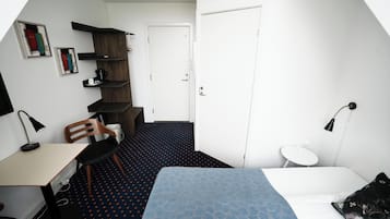 Ett litet rum med en säng, ett skrivbord, en stol, ett litet bord och en bokhylla.