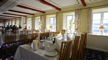 A dining area with tables set for service, wooden chairs, and a view of the outdoors through large windows.