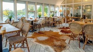 A restaurant with wicker chairs, wooden tables, and a large cowhide rug. - Hotel Årslev Kro (Aarhus)