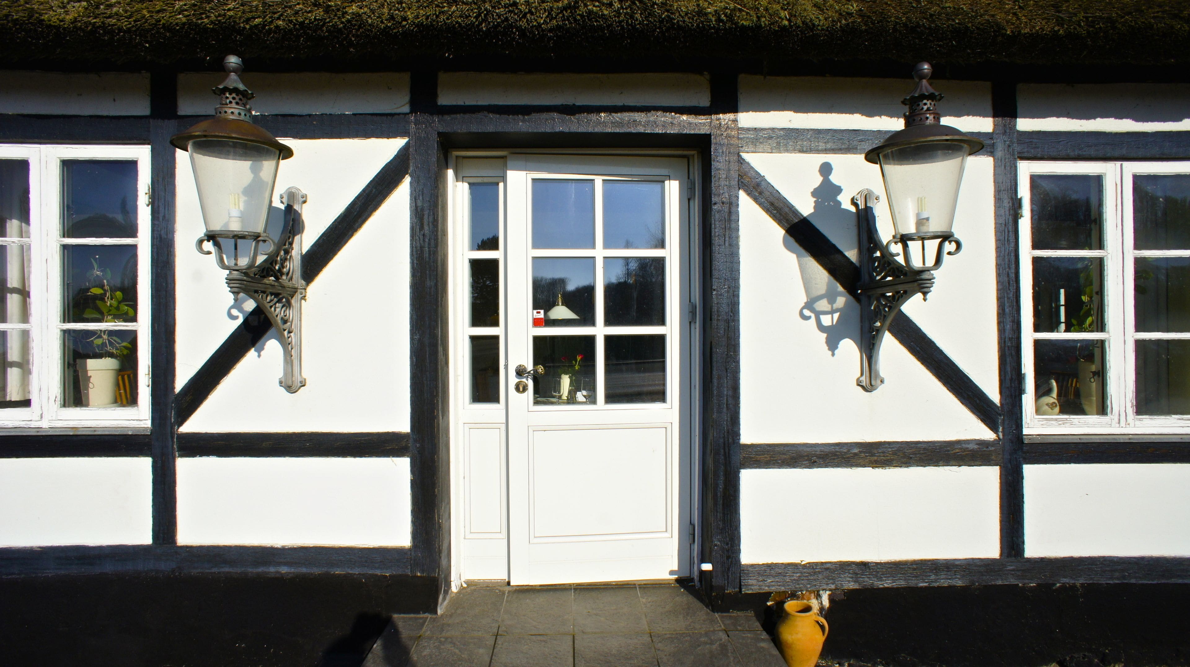 A building with a white door and black trim, two hanging lanterns, and a small dog at the entrance.