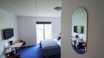 A hotel room with a bed, a desk with a chair, a television, and a large mirror.