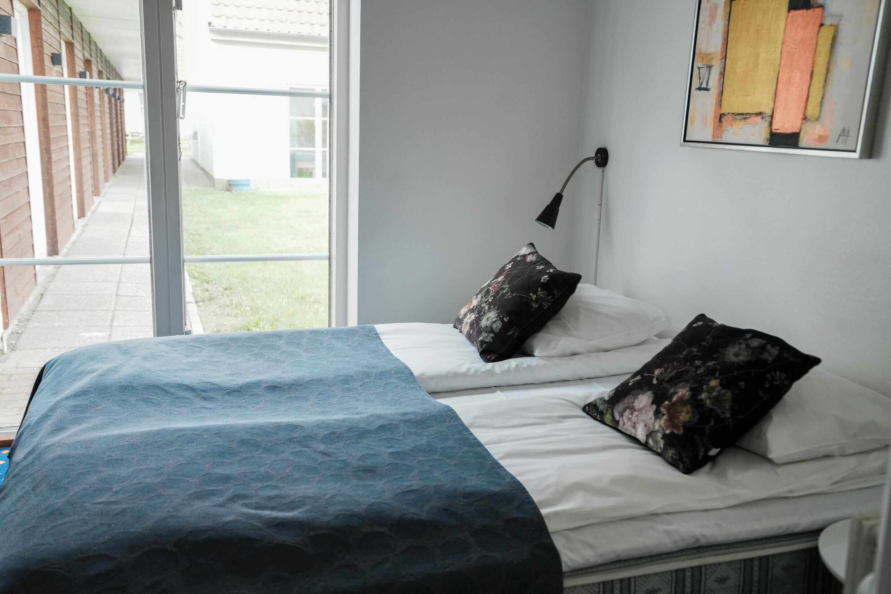A bedroom with a bed, pillows, a lamp, and a painting on the wall.