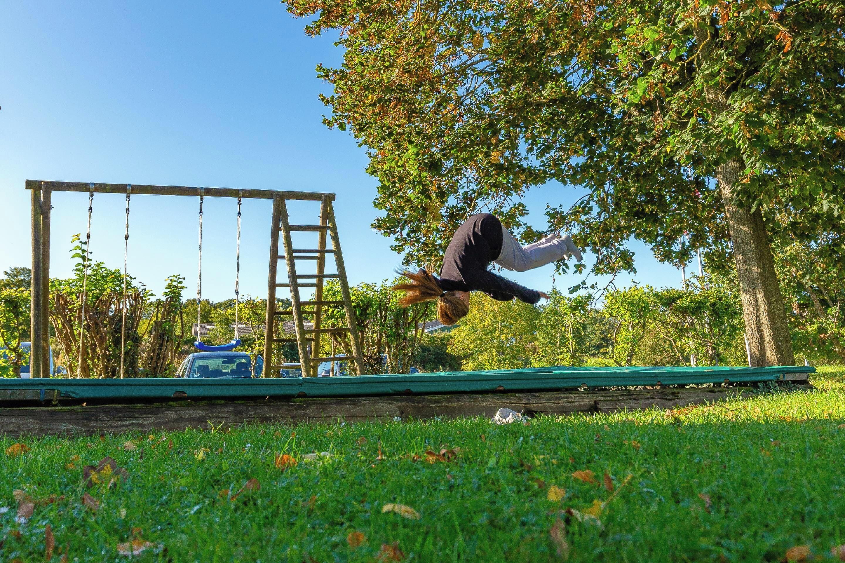 A person performing a handstand on a grassy area with a swing set and a ladder in the background.