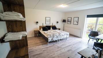 A bedroom with a bed, bedside tables, a wooden shelf with towels, a radiator, and a window with a view.