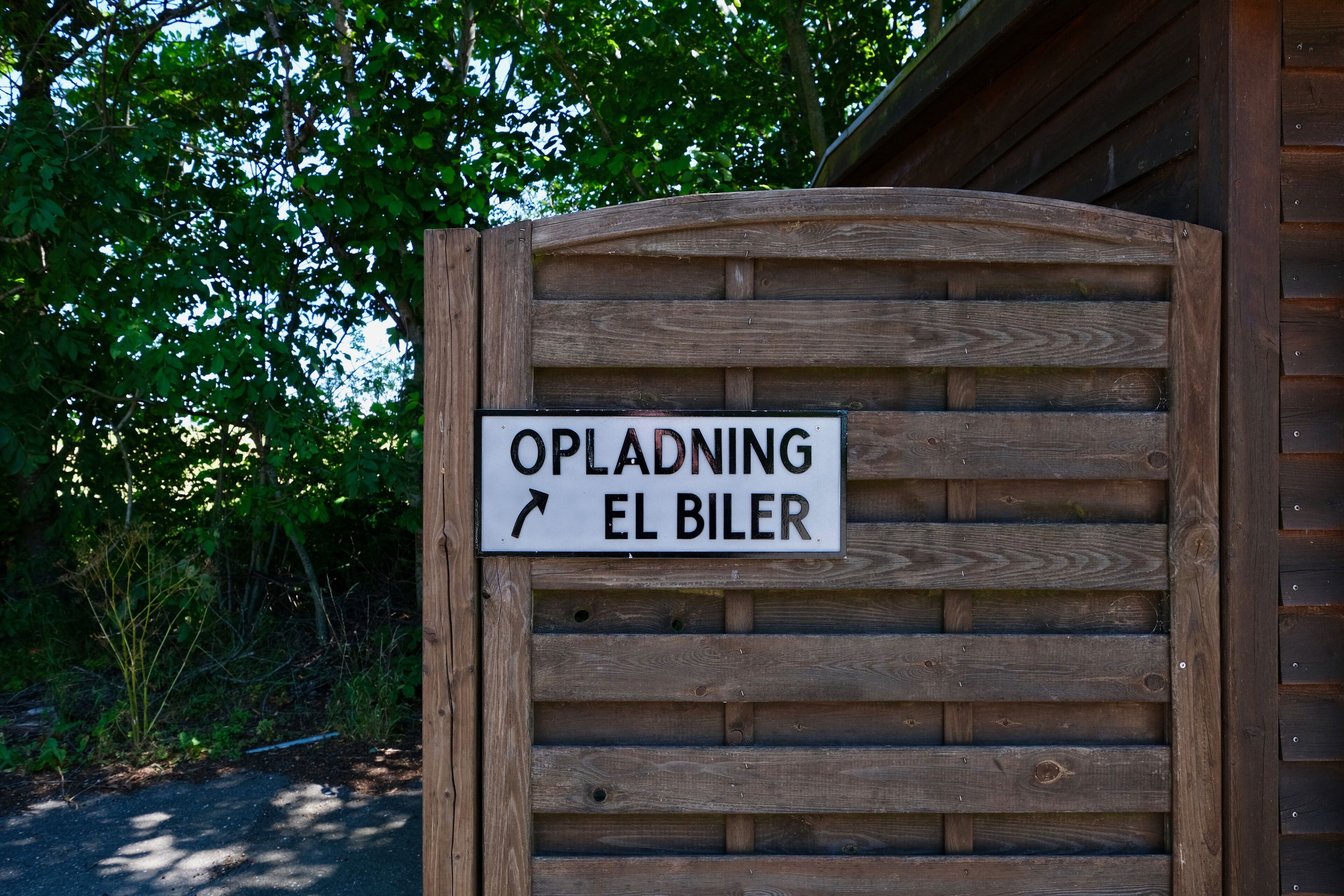 A wooden gate with a sign that reads "Opladning El Biler" and an arrow pointing right.